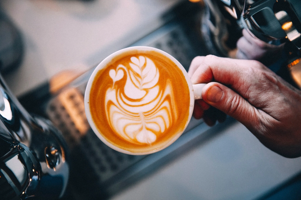 Taza de café con latte art sostenida junto a una máquina espresso
